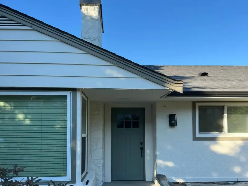 The same house front after repainting, with light walls, white trim and a green-grey front door