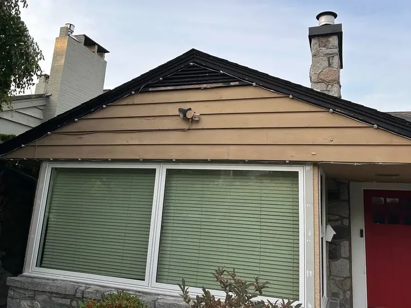 Front of a house before repainting, with faded tan siding, worn trim and a red front door