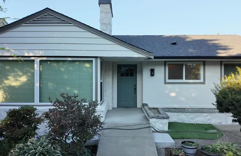 Painted house front with a teal door and shrubs along the path